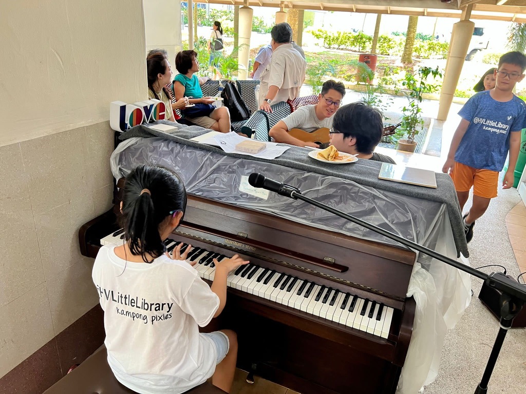 A musician plays the library piano while another plays guitar nearby